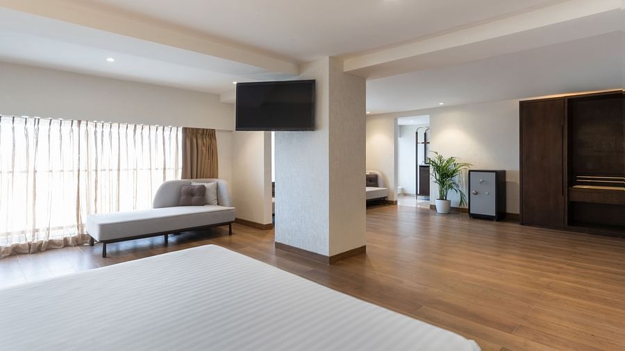 Spacious suite interior with bed in foreground, wall-mounted TV, sitting area, wooden floors, and a wardrobe at Clarks Inn Suites, Hyderabad