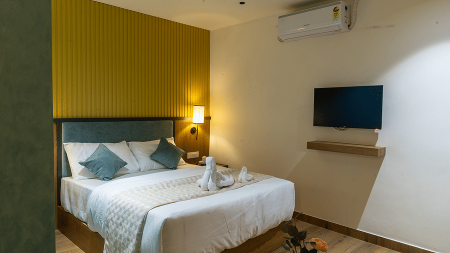 Cosy hotel room featuring a king-sized bed, wall-mounted television, and air conditioning unit.