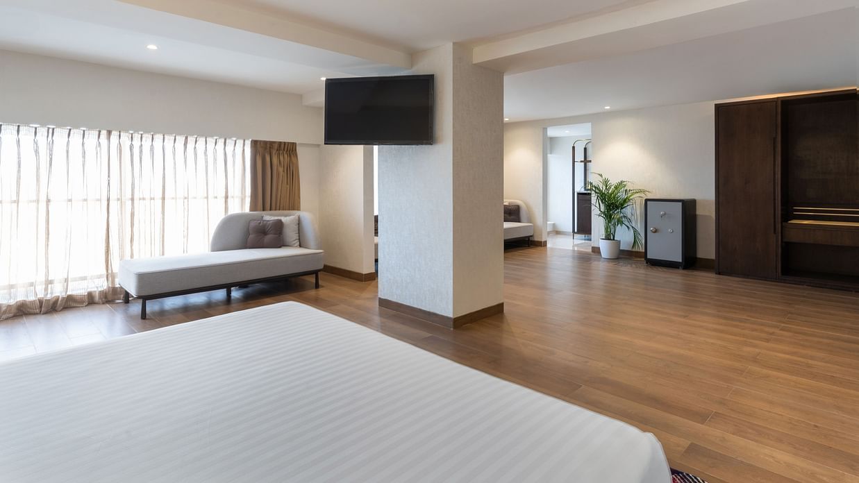Spacious suite interior with bed in foreground, wall-mounted TV, sitting area, wooden floors, and a wardrobe at Clarks Inn Suites, Hyderabad