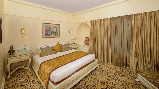 Premium Suite at Pride Hotel Pune featuring a plush king bed on a patterned floor with nightstands on both sides and a large window with curtains on next to it