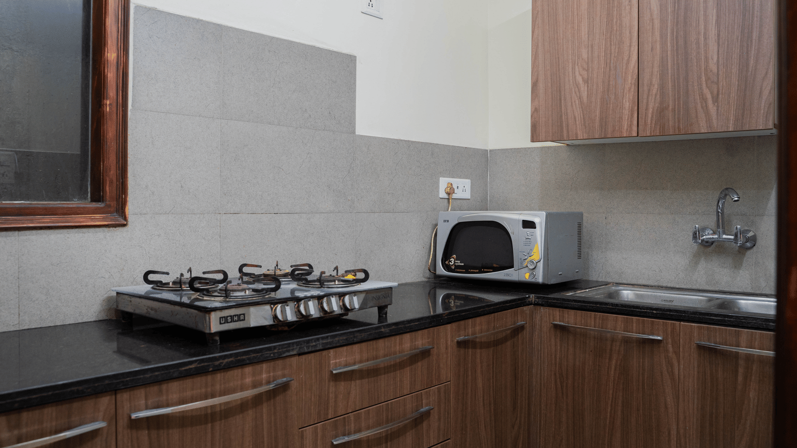 A kitchen area with a gas stove, microwave, sink, and wooden cabinets on a counter at Perfectstayz Value Shimla (Namah Retreat).