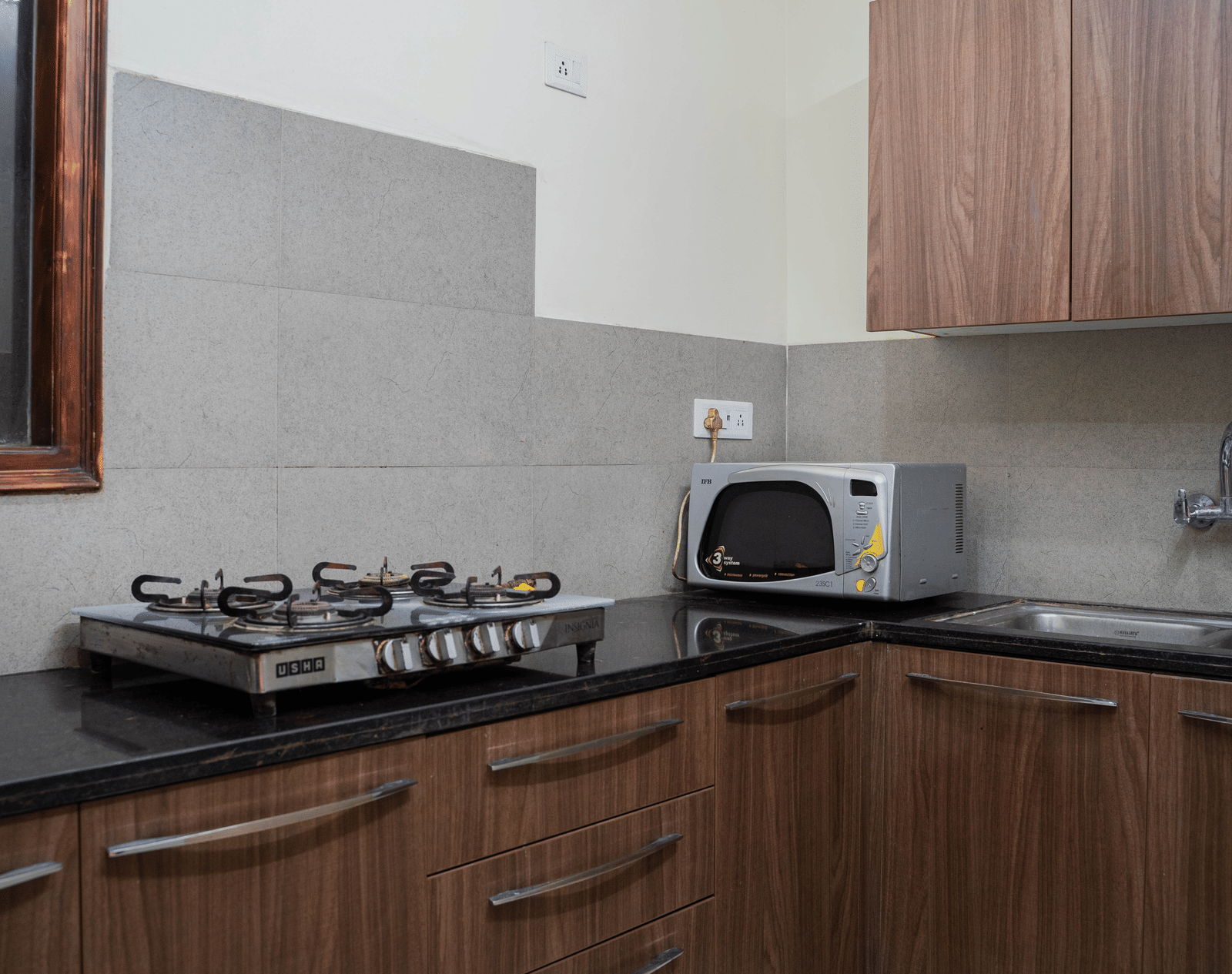 A kitchen area with a gas stove, microwave, sink, and wooden cabinets on a counter at Perfectstayz Value Shimla (Namah Retreat).