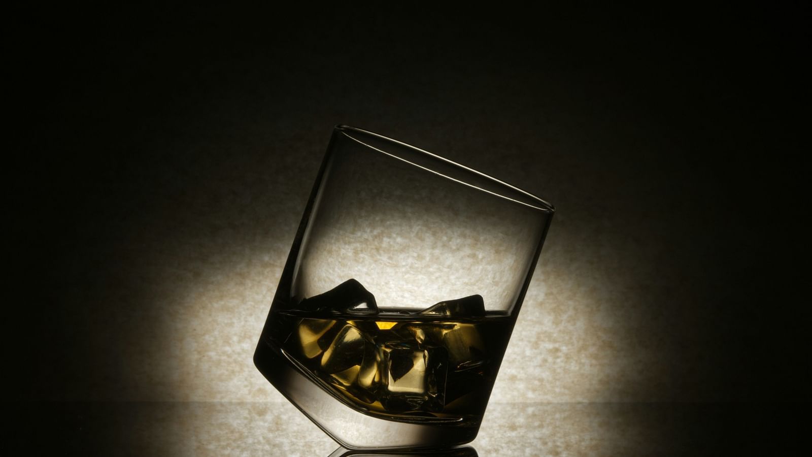 An overview of a glass with ice and whisky in it with a spotlight on the glass.