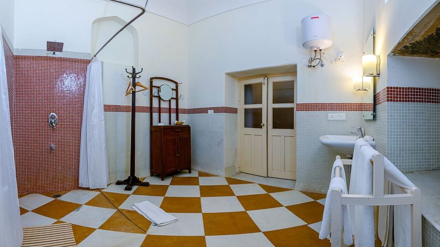 A bathroom with a sink, a door, a shower curtain, a cabinet with a mirror, a towel rack, and a checkered floor at Tijara Fort-Palace - 19th Century, Alwar.