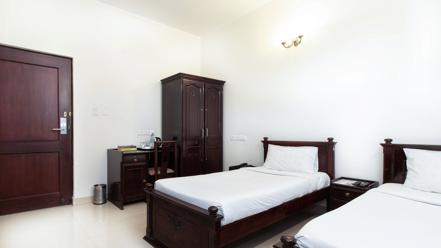 Twin bedroom with two beds, white linen, and a dark wooden wardrobe at Sanctum Suites Indiranagar, Bangalore.