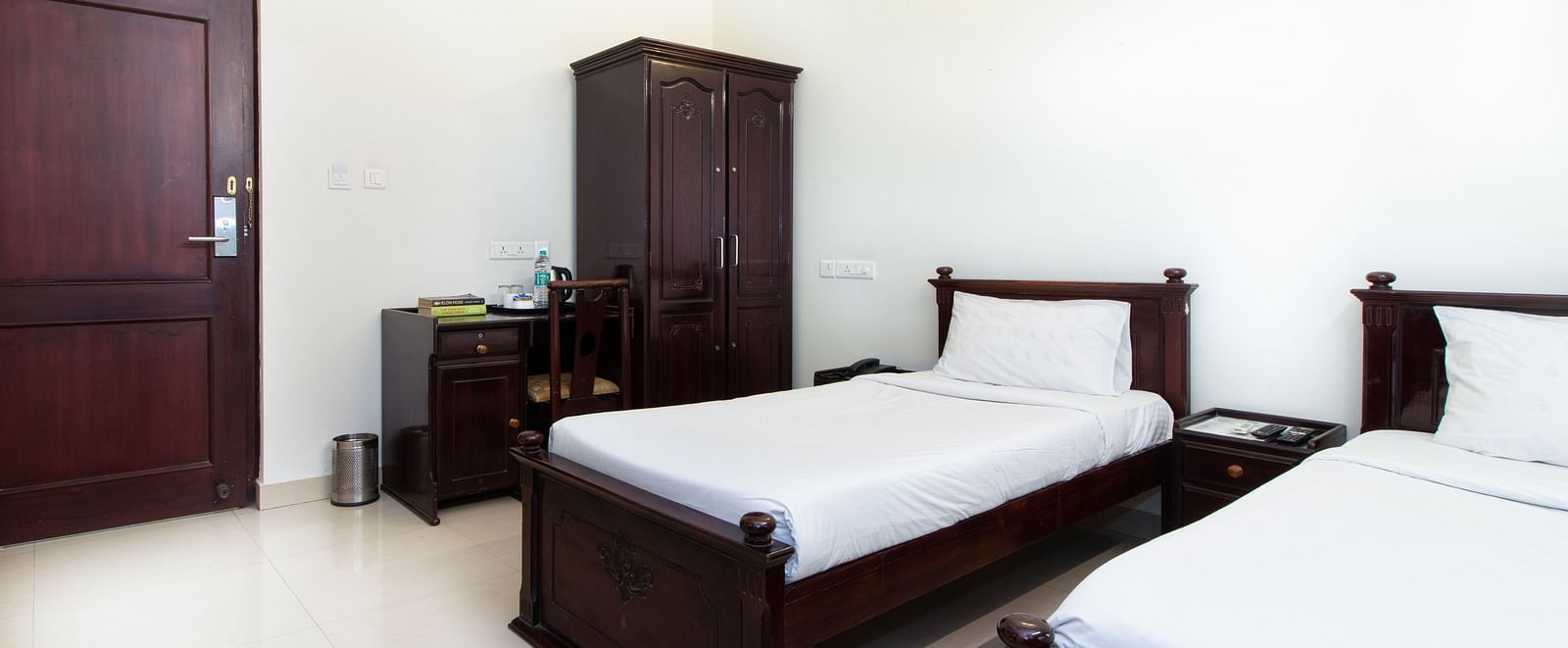 A room with twin beds featuring white bedding, a wardrobe, bedside tables, and soft lighting for a comfortable stay at Sanctum Suites Indiranagar, Bangalore.