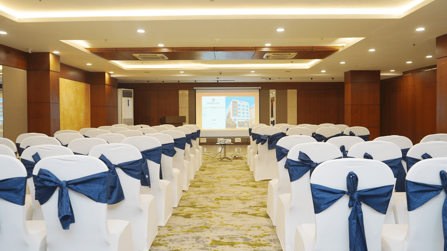Rows of white and blue chairs setup in theater style facing a projection screen at the front of a seminar room.