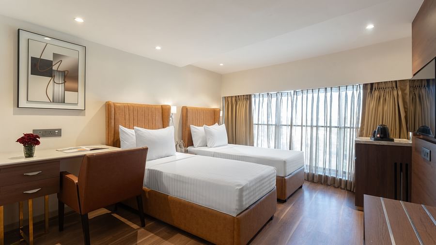 Spacious twin bed hotel room with floor-to-ceiling curtains, desk area and contemporary furnishings at Clarks Inn Suites, Hyderabad