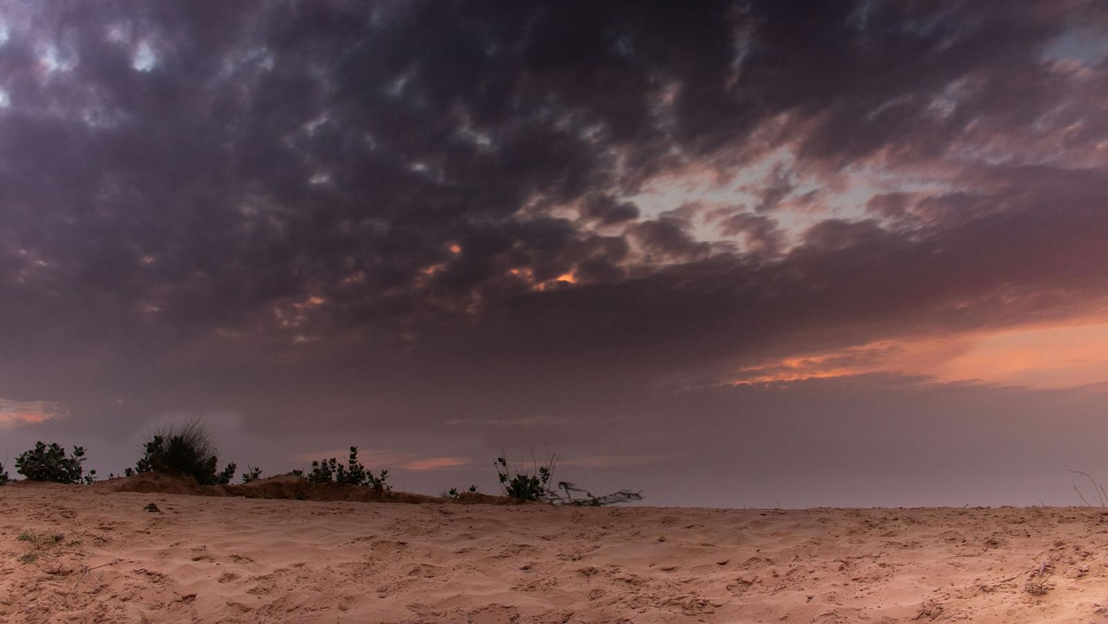 A sandy dessert on a cloudy sky during sunset.