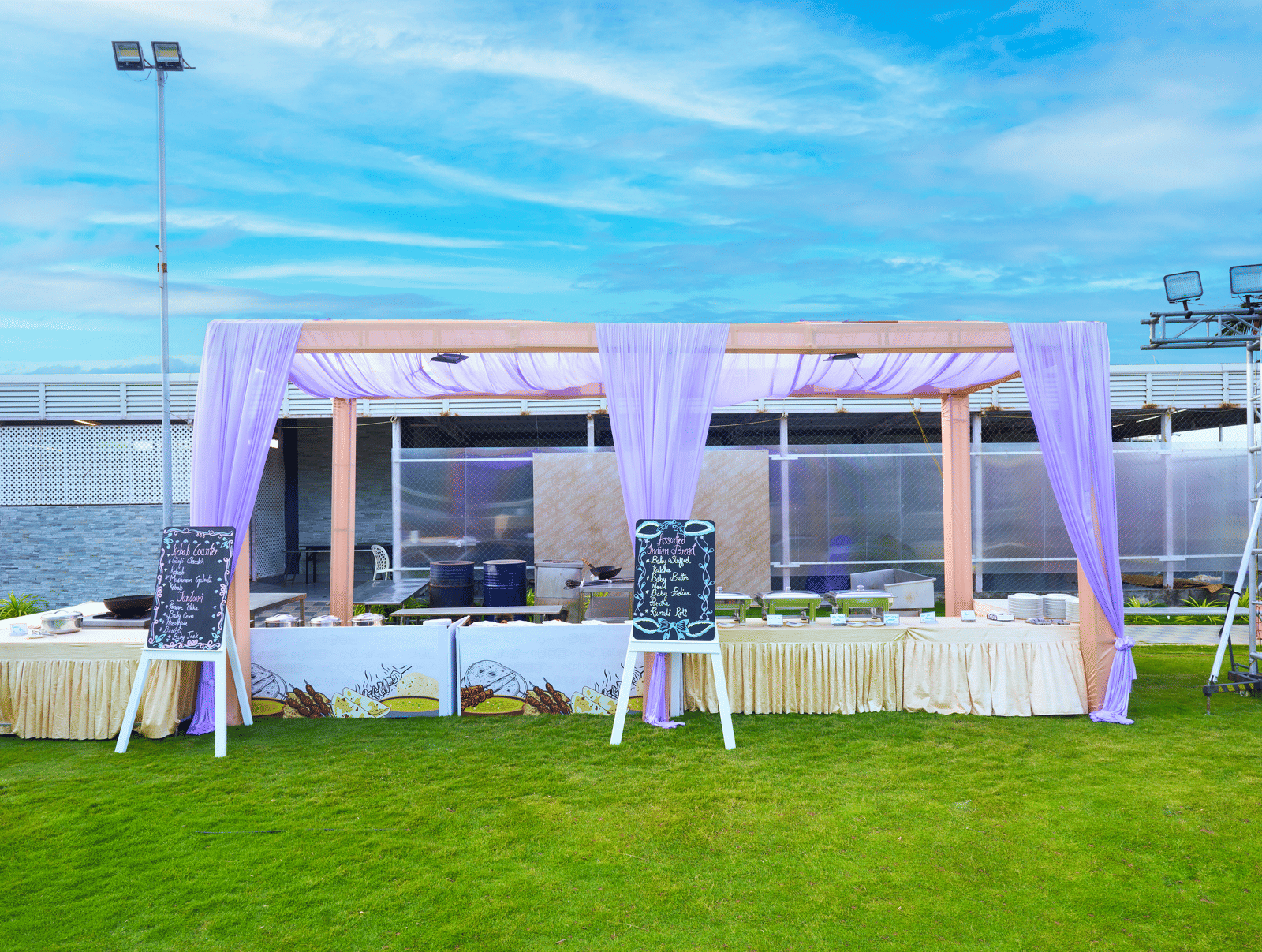 A soft pink draped outdoor canopy area featuring a buffet setup at Grande Bay Resort & Spa, Mamallapuram.