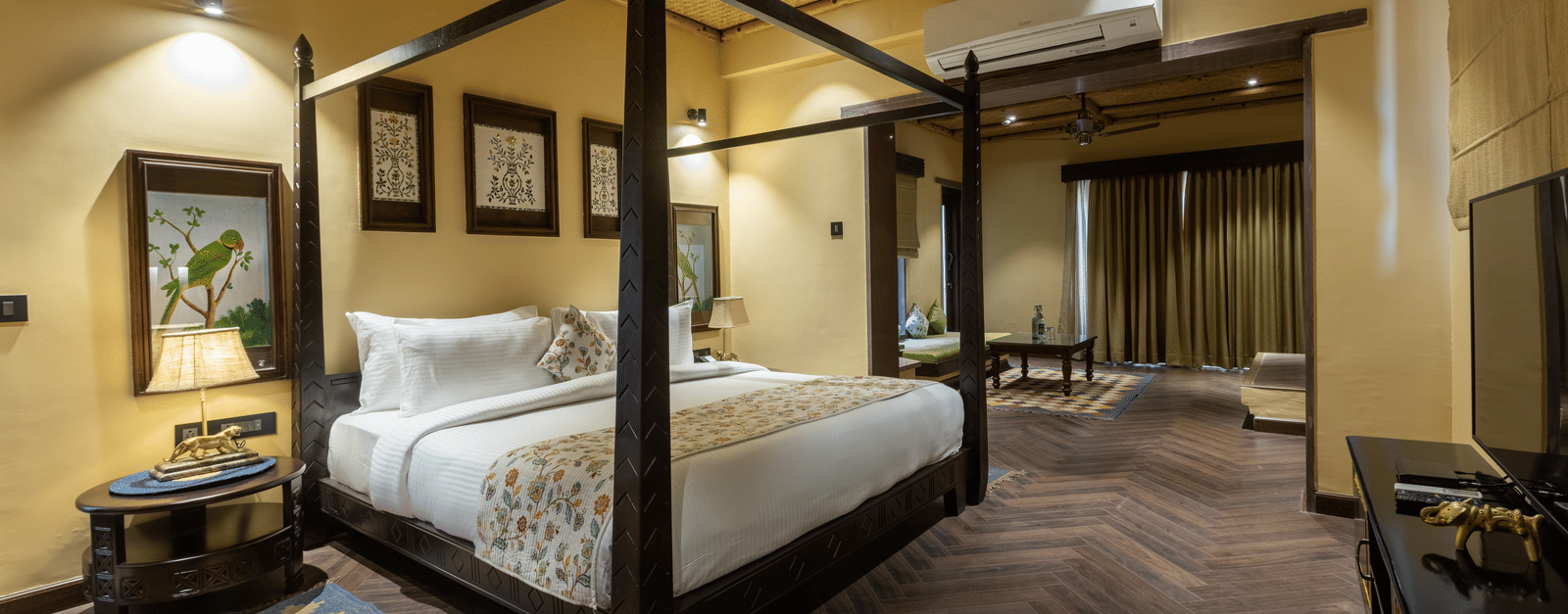 A refined bedroom at Aamaghati Wildlife Resort with a four poster bed, warm lighting, and elegant interiors offering a restful retreat.