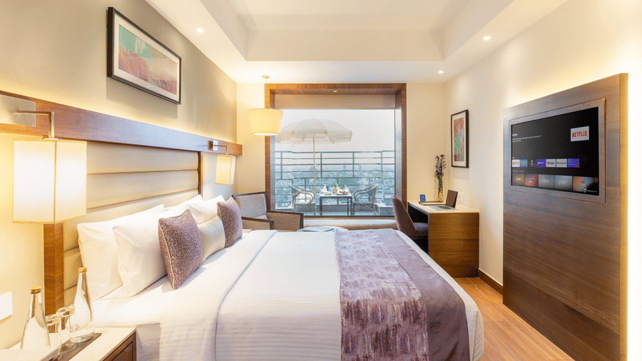 A bedroom at Nirvana Sarovar Portico, Gorakhpur featuring a king size bed, a study desk, a television, and access to a balcony.