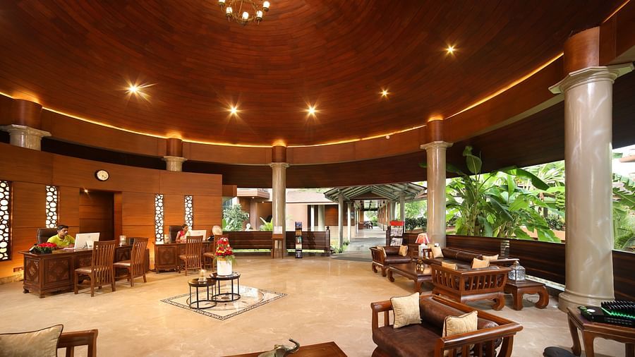 The lobby area at Uday Backwater Resort features warm lighting, a wooden ceiling, elegant seating, and open views of lush greenery, creating a relaxing ambience