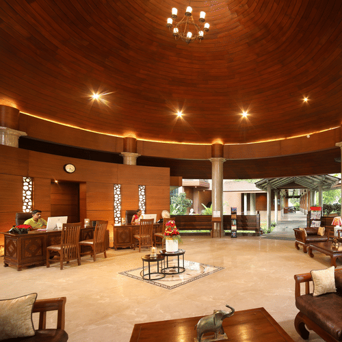 Lobby area at Uday Backwater Resort under warm lighting with wooden ceiling, elegant seating, warm lighting, and open views of greenery for a relaxing ambience