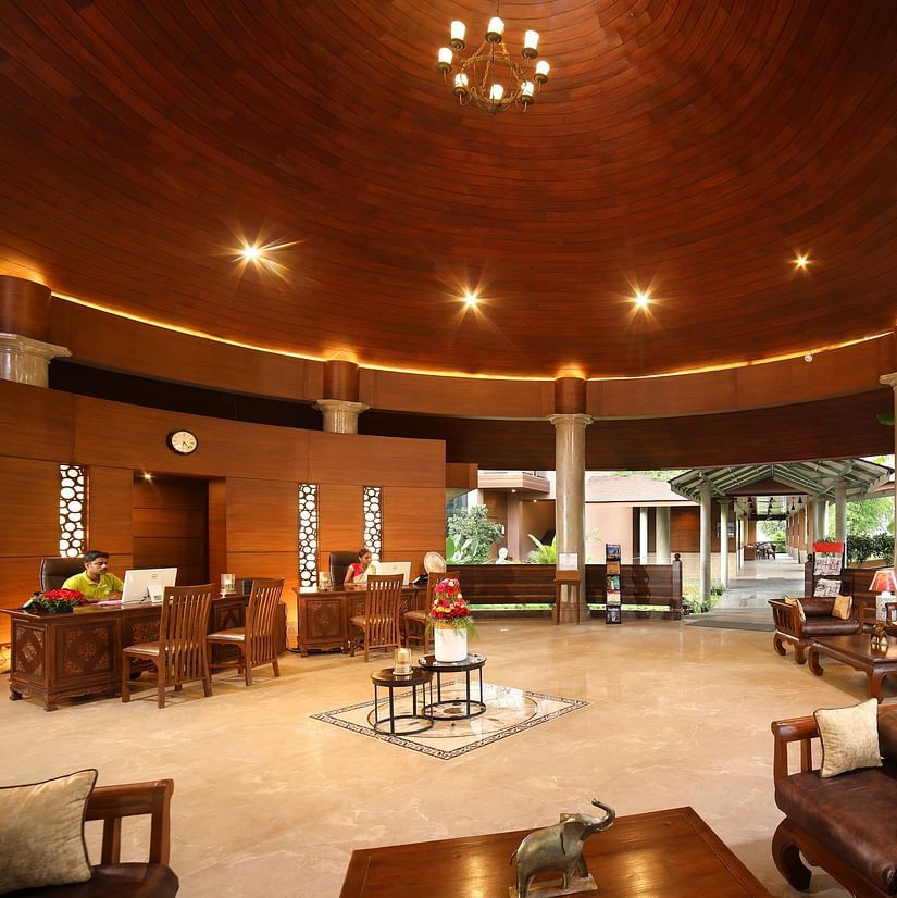 Lobby area at Uday Backwater Resort under warm lighting with wooden ceiling, elegant seating, warm lighting, and open views of greenery for a relaxing ambience