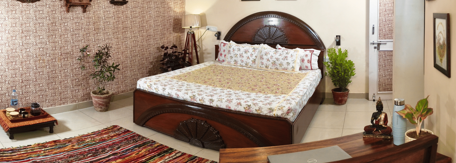 A room with a double bed, low table, chairs and wall decorations with framed items at Jaypore360 Homestay in Jaipur.