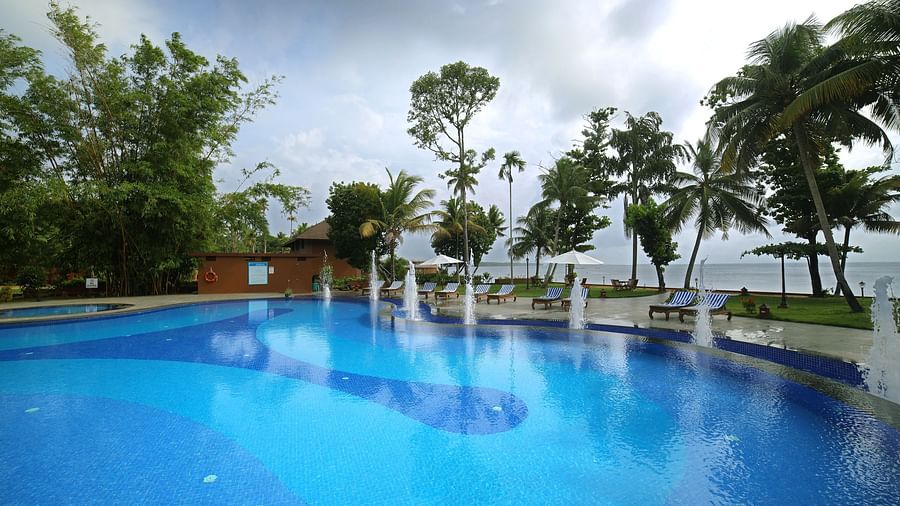 Swimming pool at Uday Backwater Resort under a cloudy sky surrounded by lush trees