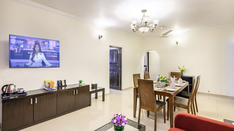 The dining area of our apartment accommodation featuring a dining table, a wall-mounted television, a couch and a coffee table, and ambient lighting - Golden Tulip, Candolim, Goa