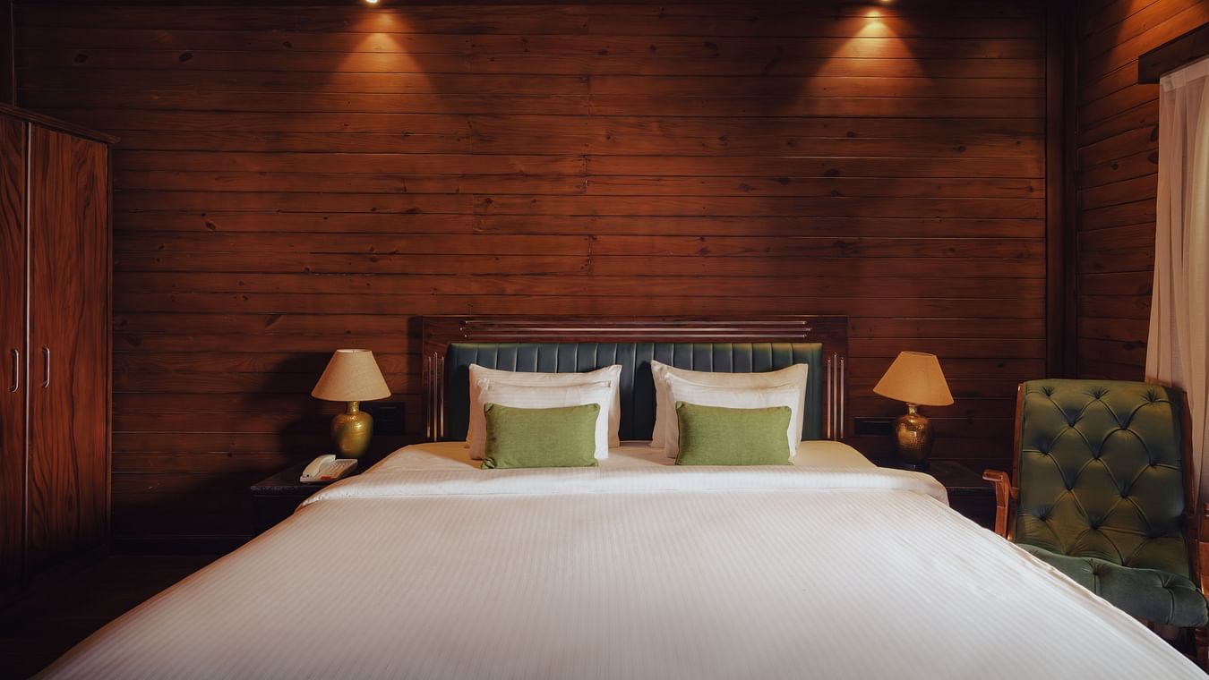 A front view of room at The Ananta Udaipur with a king sized bed, wooden walls, and bedside lamps.