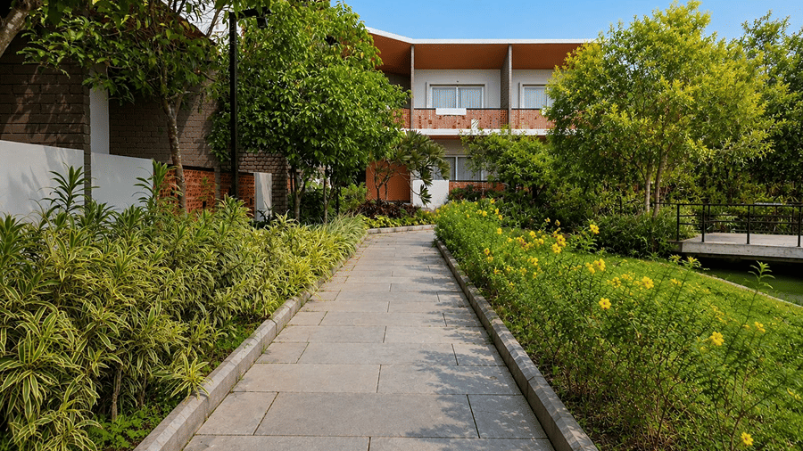 A stone walkway at Hotel Sonar Bangla, Mayapur, featuring surrounding green plants, flowering bushes, and resort buildings.