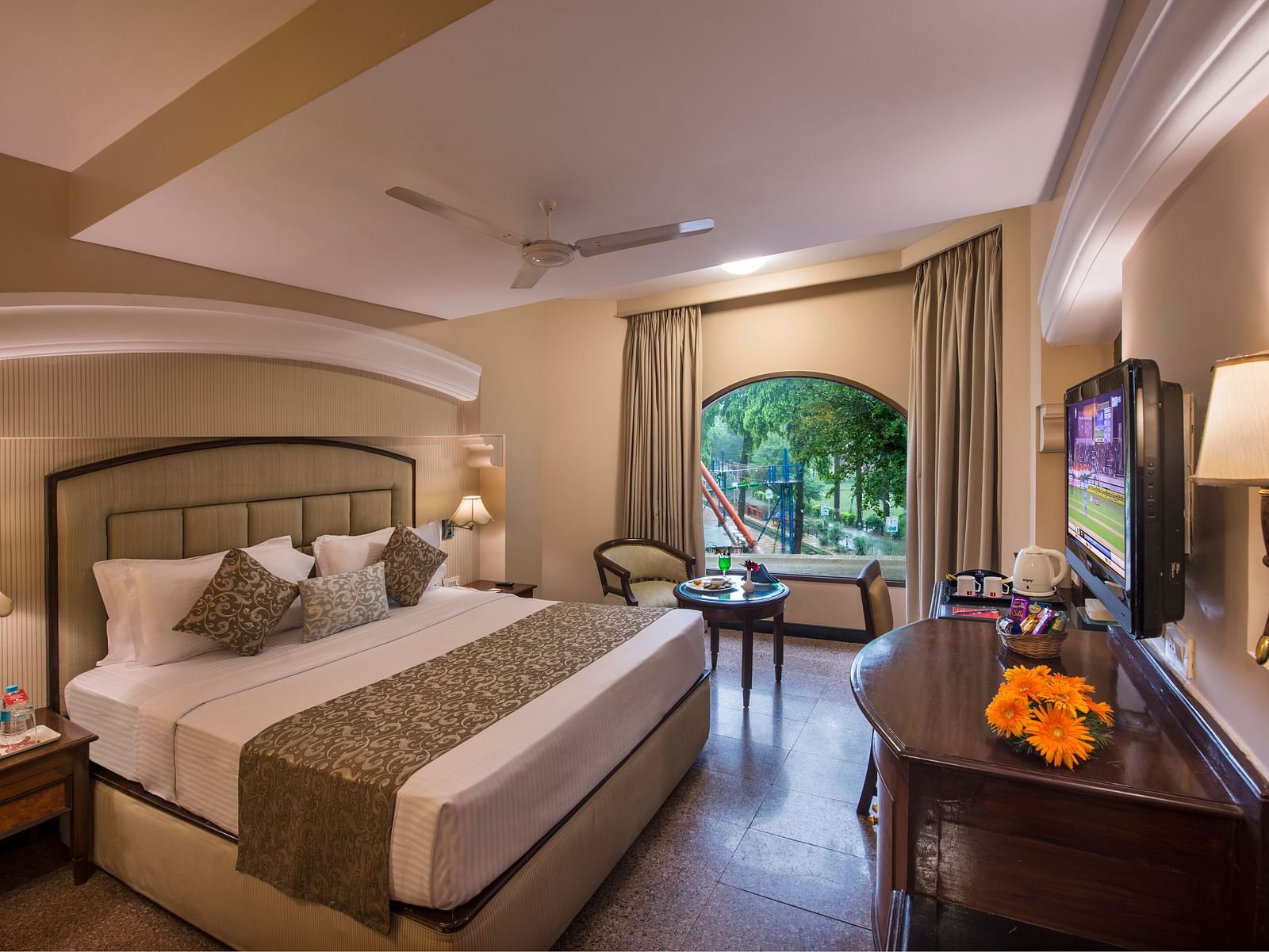 Hotel room with a neatly made bed, a decorative lamp, and a view of greenery through a window - Lords Inn Vadodara