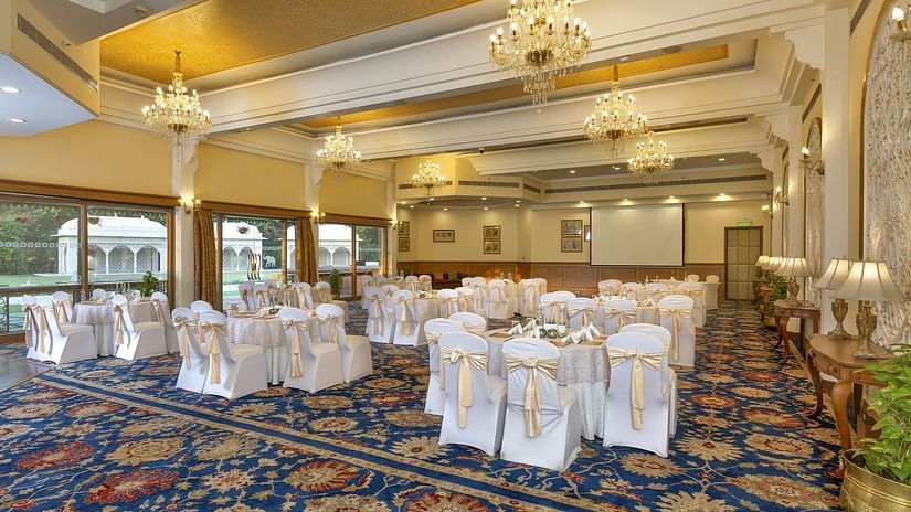 Elegant banquet hall with chandeliers, round tables draped in white, and a patterned blue carpet - Heritage Village Resorts & Spa.
