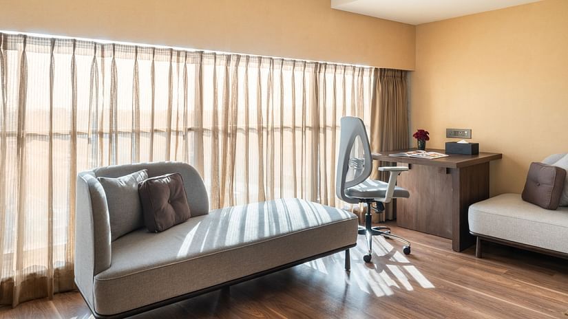 Bright corner of a room with floor-to-ceiling curtains, modern chaise lounge, and a work desk with an ergonomic chair at Clarks Inn Suites, Hyderabad