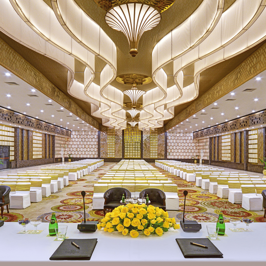 Banquet hall at The Bristol Hotel, Gurgaon set theatre style with rows of white chairs, an ornate gold ceiling, and a head table with yellow roses.