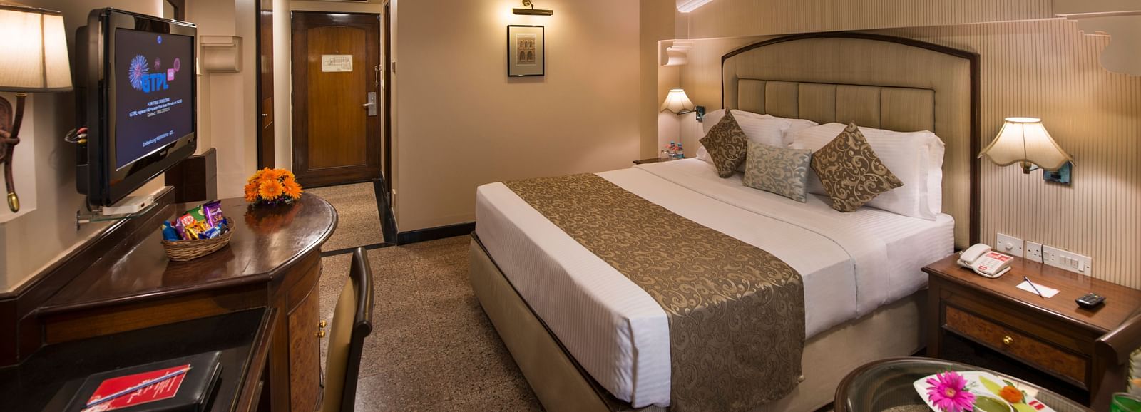 Hotel room with a bed, a nightstand, a TV, and a view into the bathroom - Lords Inn Vadodara