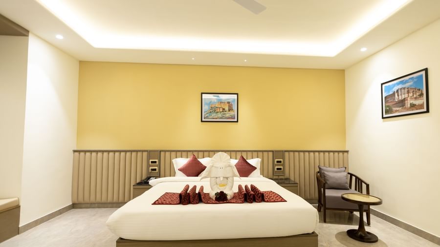 A tidy hotel room at Pride Resort, Jodhpur, with a large bed, decorative cushions, towel art, and framed artwork on the walls.