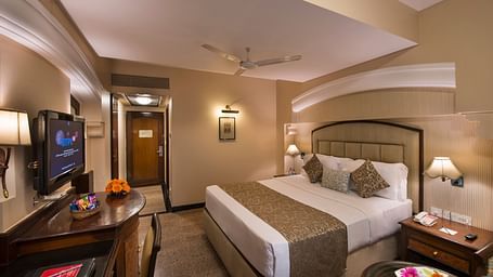 Hotel room with a bed, a nightstand, a TV, and a view into the bathroom - Lords Inn Vadodara