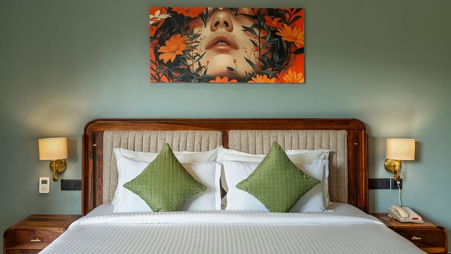 Valley View Room with a painting above a king size bed, bedside lamps, and green pillows at The Qualia Resort Club & Brewery, Udaipur.