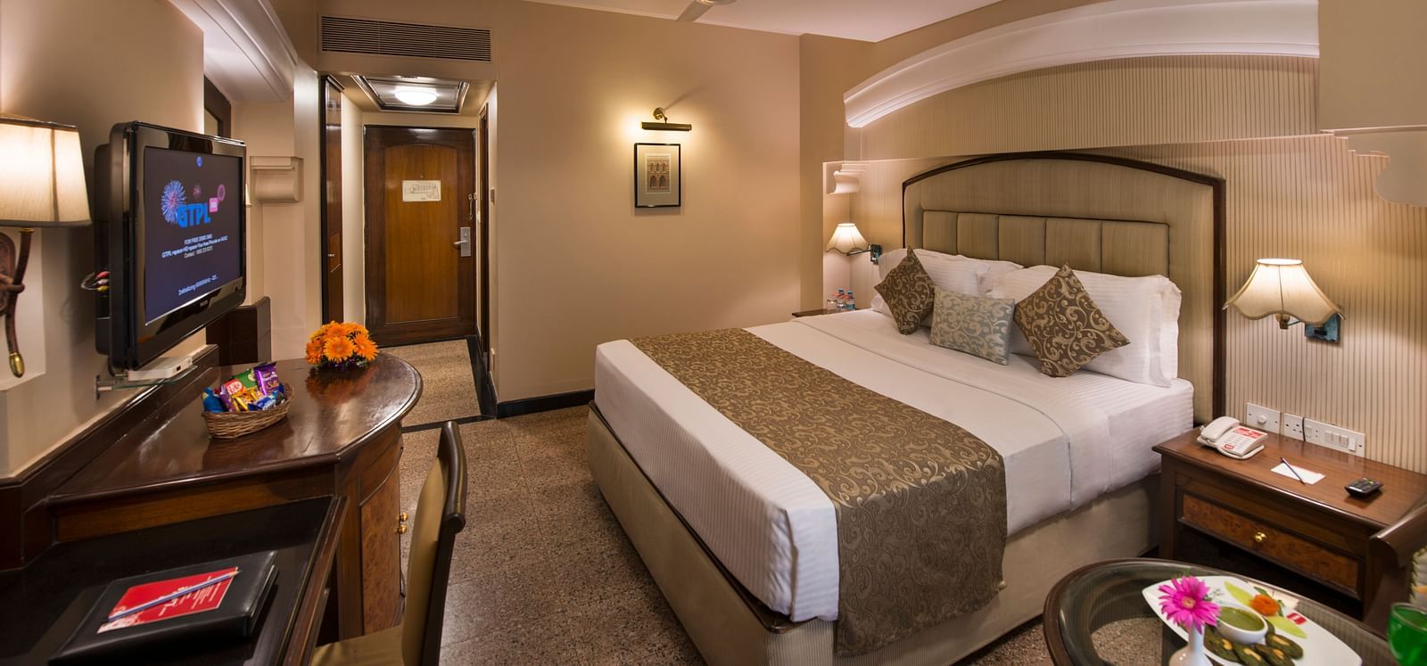 Hotel room with a bed, a nightstand, a TV, and a view into the bathroom - Lords Inn Vadodara