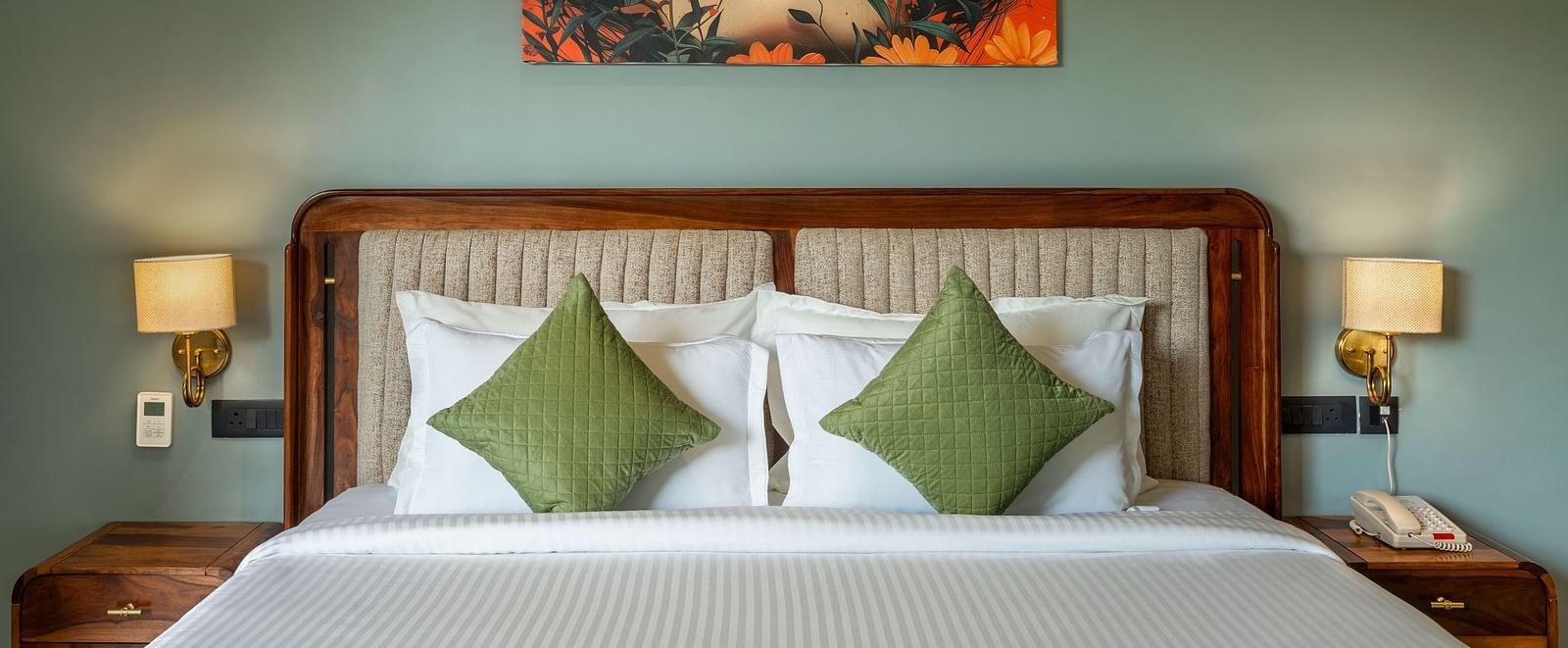 Valley View Room with a painting above a king size bed, bedside lamps, and green pillows at The Qualia Resort Club & Brewery, Udaipur.