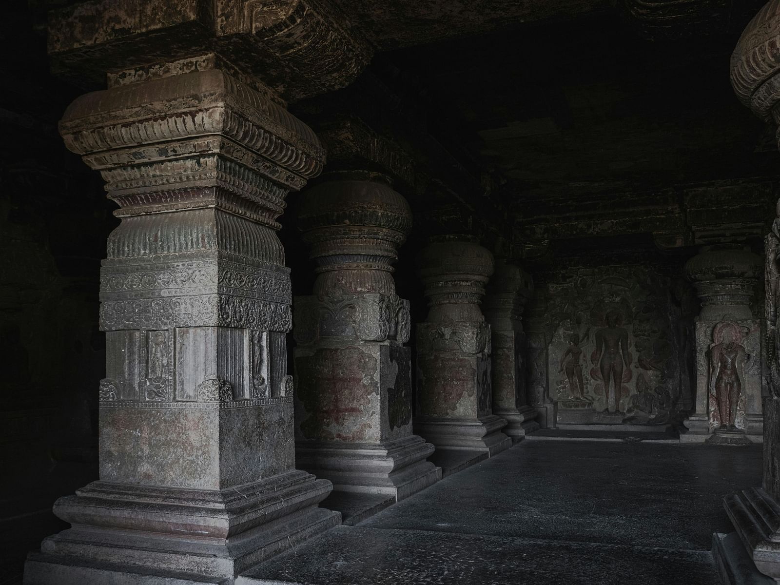 A dark, ancient cave interior with large, intricately carved stone pillars and statues