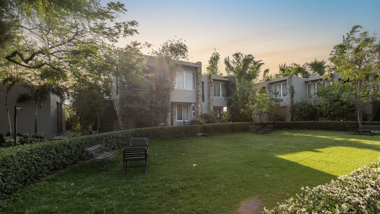 A lush green lawn surrounded by trees and villa buildings under a sunny sky  at The Golden Tusk, Jim Corbett