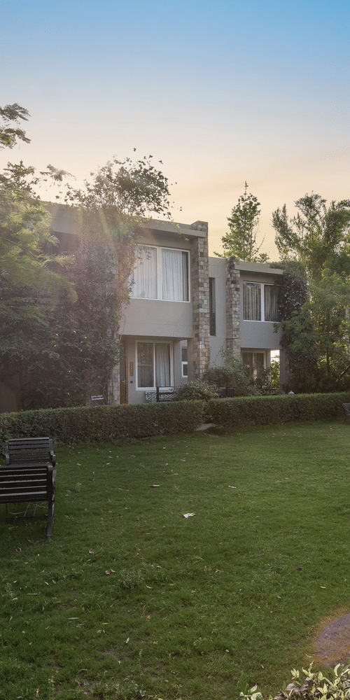 A lush green lawn surrounded by trees and villa buildings under a sunny sky  at The Golden Tusk, Jim Corbett