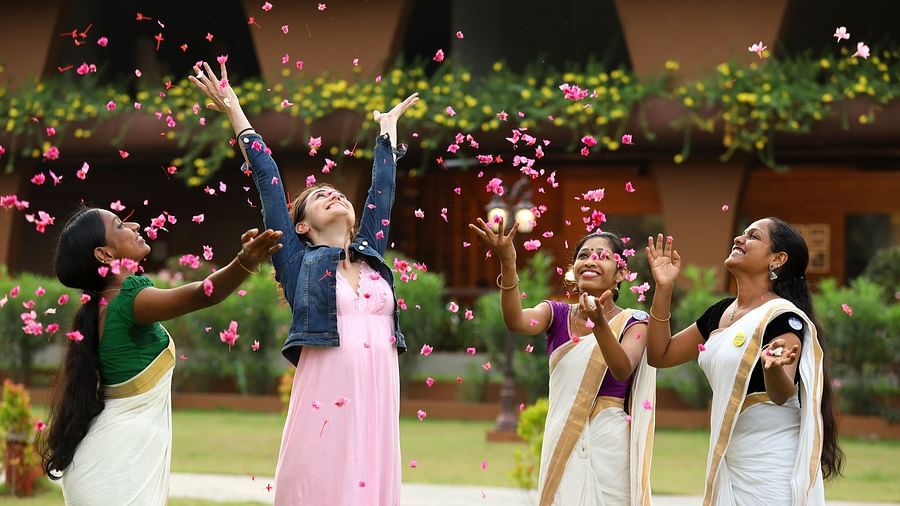 Women dressed in traditional attire joyfully tossing pink flower petals into the air, celebrating amidst green surroundings at Uday Backwater Resort