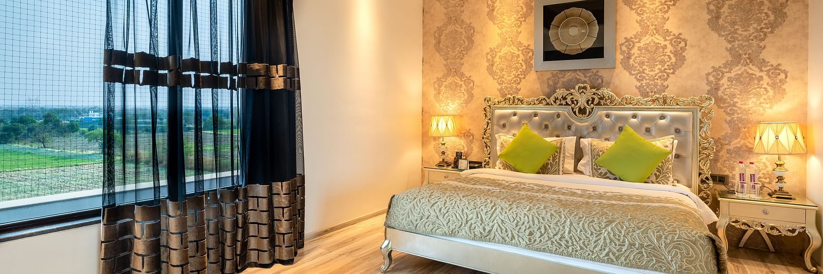 Spacious bed with a photo frame above the headboard, a bedside table with warm lighting, and a large window to the side at Crescent Spa & Resort, Indore
