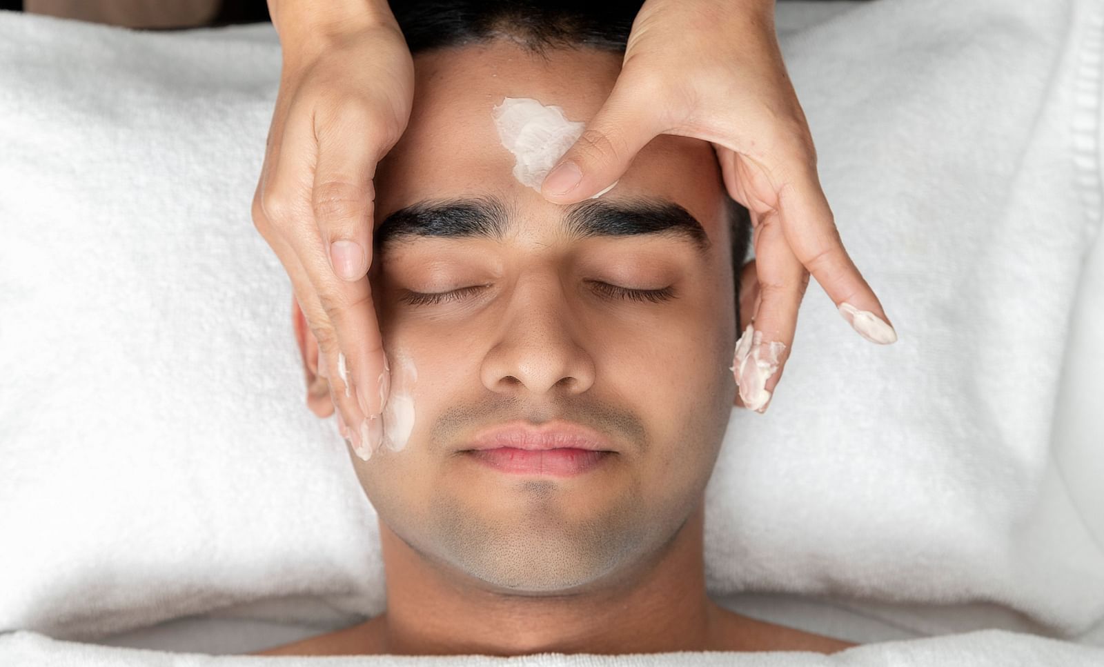 A man enjoying a face massage from a masseuse at Cinqtuair Spa, The Claridges New Delhi