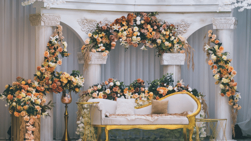 Exquisite wedding stage adorned with pastel floral arrangements, decorative white columns, elegant seating, and cascading floral decor, creating a sophisticated backdrop for wedding celebrations.