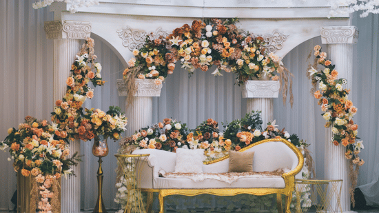 Exquisite wedding stage adorned with pastel floral arrangements, decorative white columns, elegant seating, and cascading floral decor, creating a sophisticated backdrop for wedding celebrations.