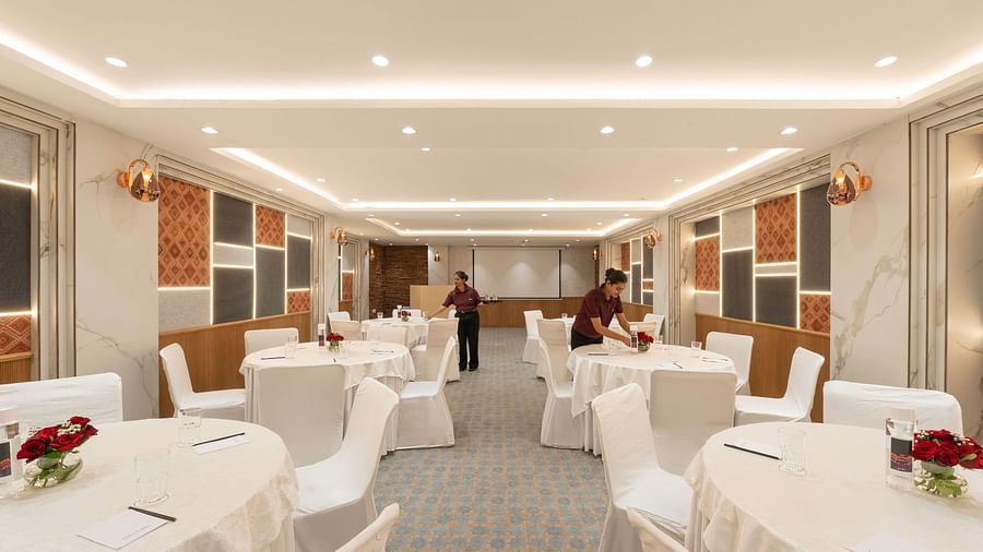 A conference room with round tables and chairs being prepared by hotel staff. The room has a modern design with decorative wall panels - Clarks Inn, Indore