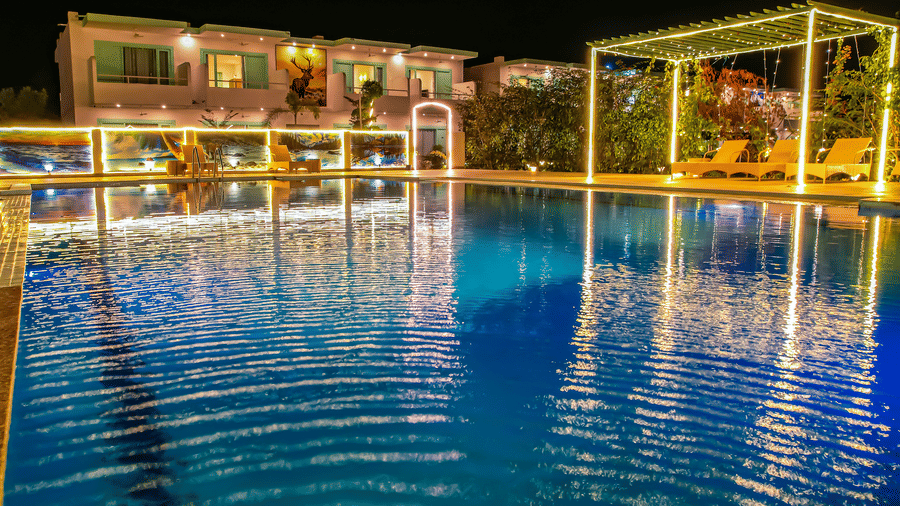 Night view of a swimming pool decorated with lights and buildings and trees can be seen in the background - Vedikant Resorts The Mallard Corbett.