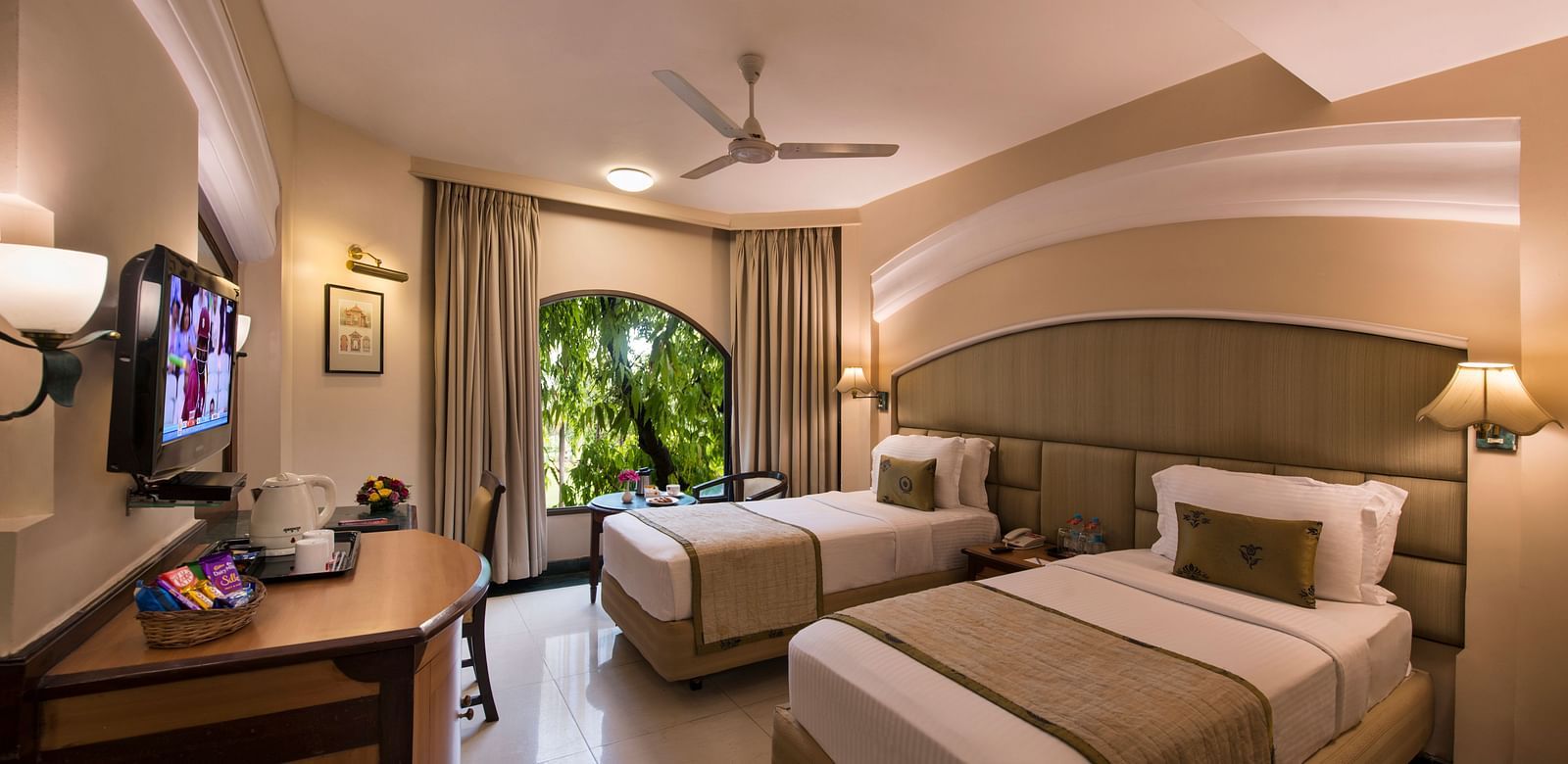 Hotel room with a striped bed runner, a TV, a ceiling fan, and a glimpse of the outside - Lords Inn Vadodara