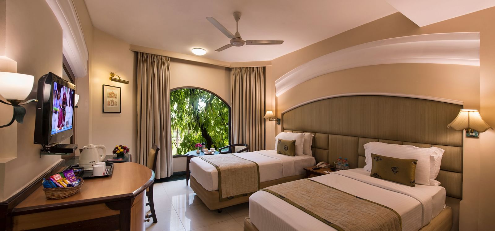 Hotel room with a striped bed runner, a TV, a ceiling fan, and a glimpse of the outside - Lords Inn Vadodara