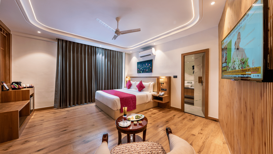 A spacious bedroom layout at Lords Inn Katra featuring a king size bed, a small round coffee table, and a comfortable upholstered armchair.
