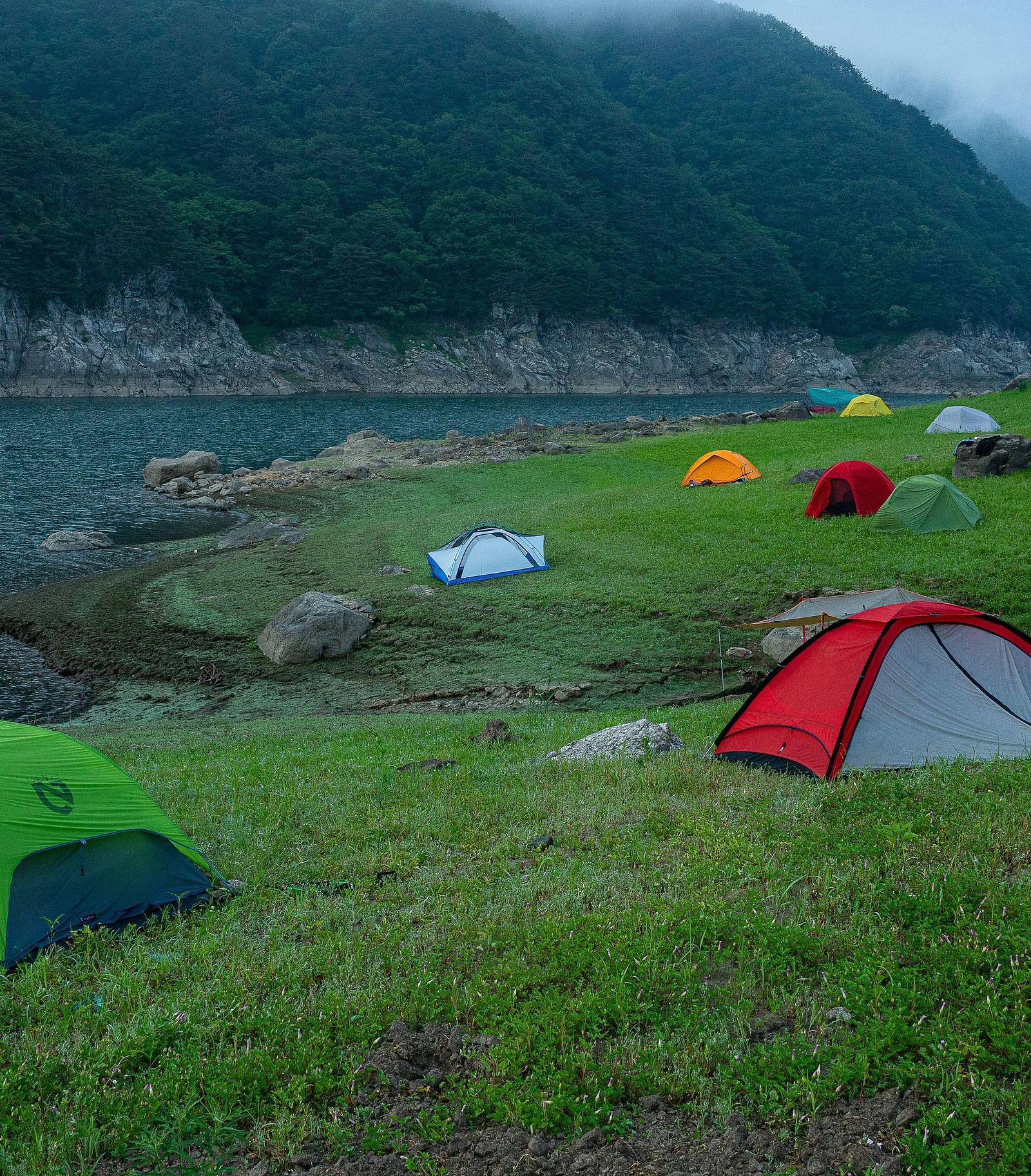 An overview of a campsite with many tents placed on the area near the lake.