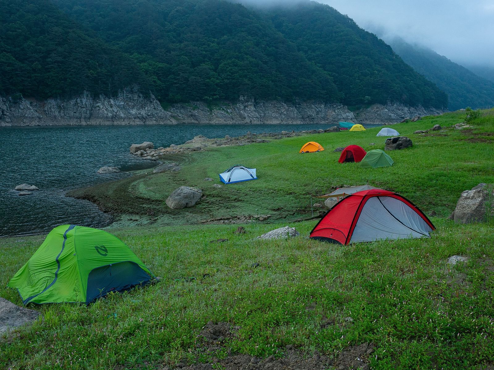 An overview of a campsite with many tents placed on the area near the lake.