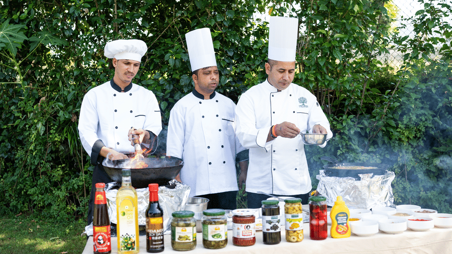 Three chefs in uniforms at Corbet Nirvana Resort  standing behind an outdoor counter with food containers and bottles.